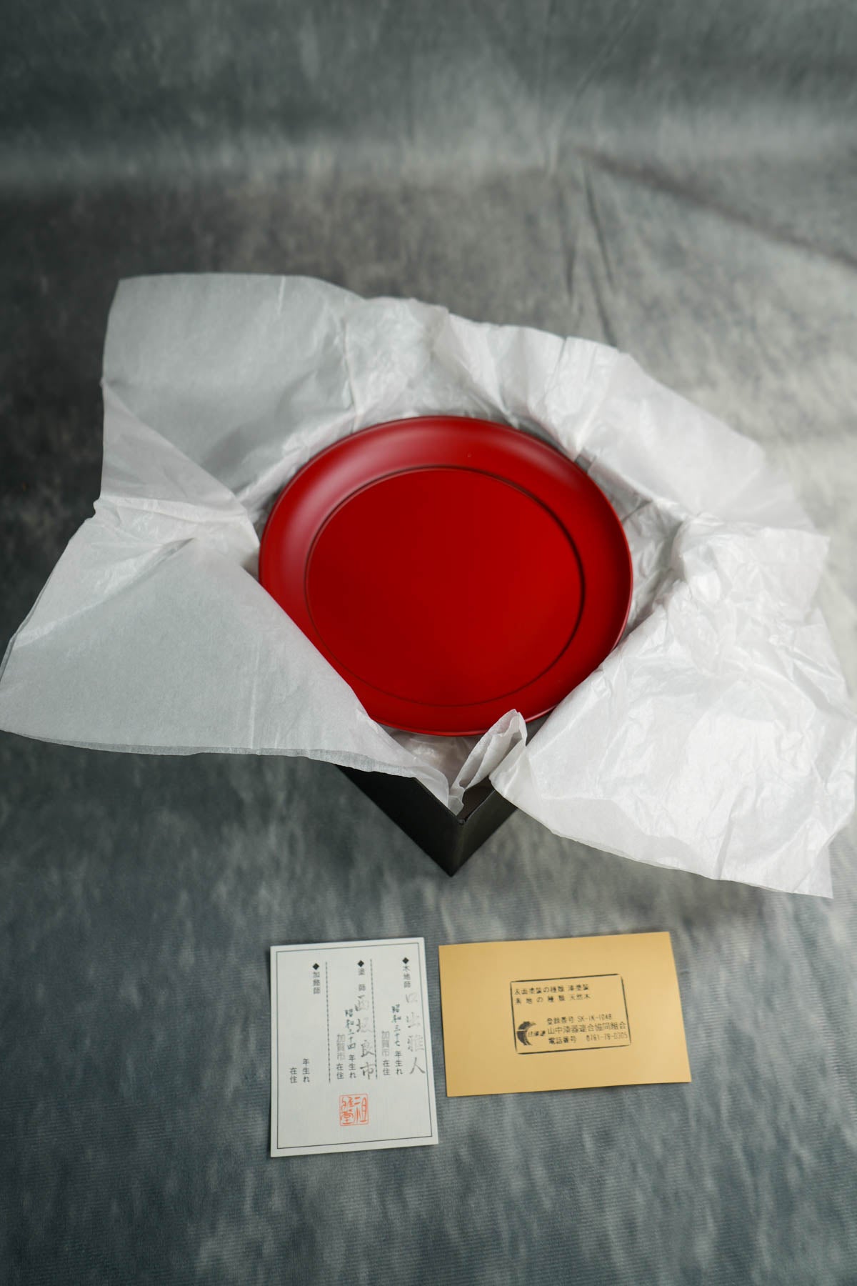 Delicately nestled within an elegant box, this set includes two plates featuring the names of skilled craftsmen, adorned with the prestigious stamp of the Japanese Lacquer Artisans Union and the manufacturer's seal.